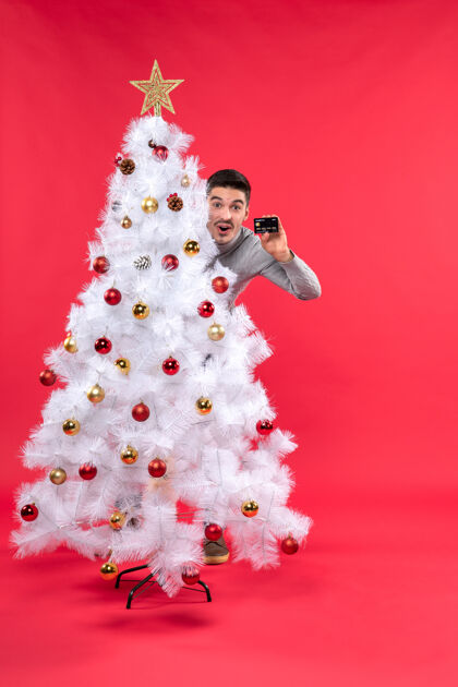 男人圣诞节心情与惊喜情绪的家伙站在装饰圣诞树后 看着他的手机礼物装饰圣诞