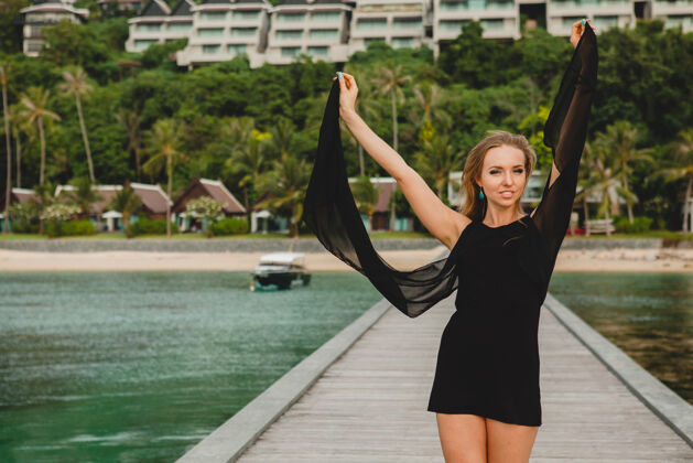 自由穿着黑色连衣裙的美丽迷人的女人在豪华度假酒店的码头上摆姿势 暑假 热带海滩岛屿年轻热带