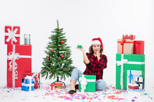 礼物正面图：年轻女子围坐在白墙上 手里拿着绿色的银行卡微笑礼物冬天