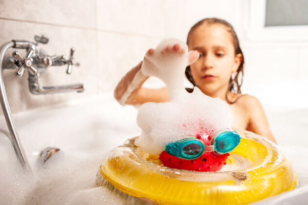 笑严肃可爱的小女孩在泡沫塑料浴缸里洗澡 玩着玩具 想象着自己去了海边孩子们的海上暑假梦想的概念人小玩具