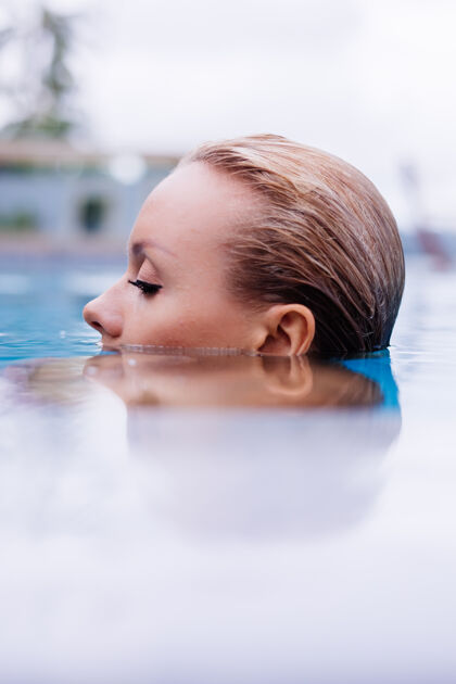 现代穿着比基尼的白种女人在蓝色游泳池的时尚写真 在coudydaynaturallight度假女士热带花园