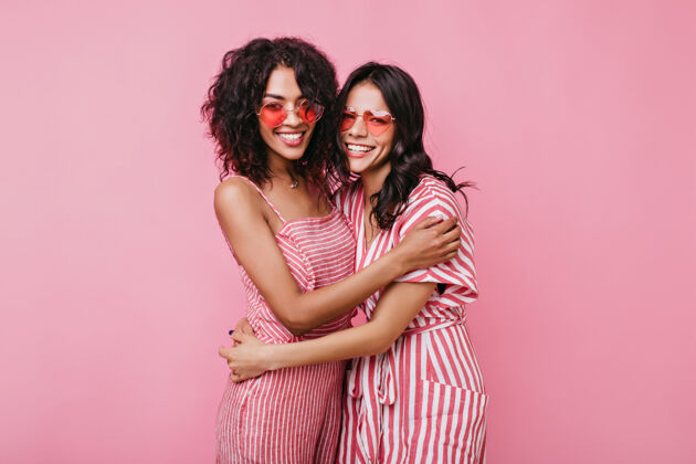 朋友可爱浪漫的女孩们友好地拥抱在一起戴着粉色太阳镜的女士们哈哈大笑成人拥抱时尚