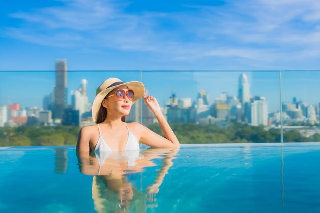 外部肖像美丽的亚洲年轻女子微笑放松休闲围绕室外游泳池与城市景观城市景观天际线身体