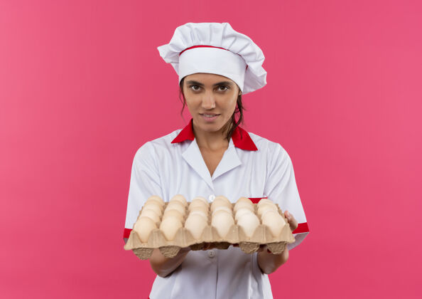 鸡蛋年轻的女厨师穿着厨师制服 拿着一批鸡蛋放在隔离的粉红色墙上 还有复制空间批抱厨师