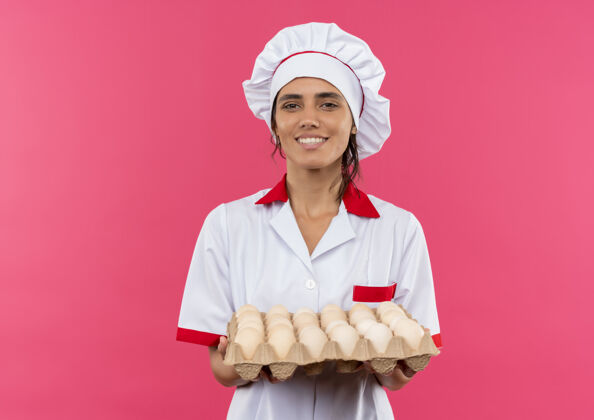 持有面带微笑的年轻女厨师穿着厨师制服拿着一批鸡蛋与复印空间女厨师穿