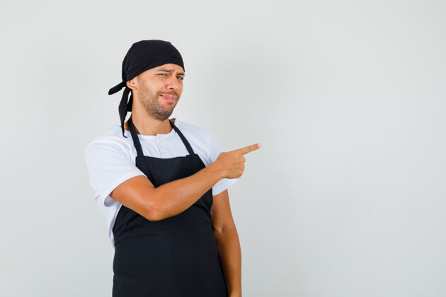 成人面包师指着旁边穿着t恤 围裙的面包师 满脸渴望新鲜制服烹饪