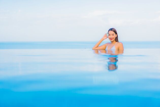 亚洲人肖像美丽的亚洲年轻女子放松微笑周围的室外游泳池在酒店度假村水帽子健康