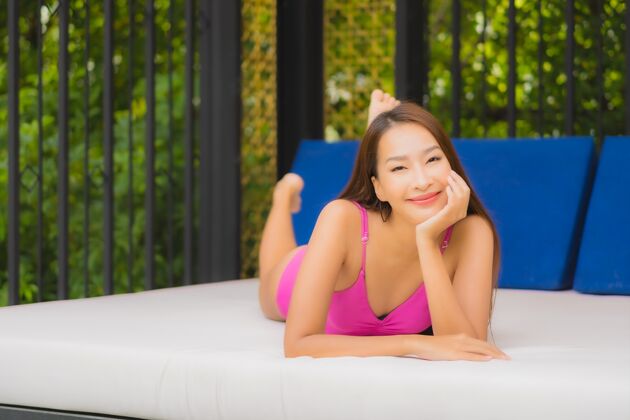 女性肖像美丽的亚洲年轻女子放松微笑周围的室外游泳池在酒店度假村休闲性感游泳