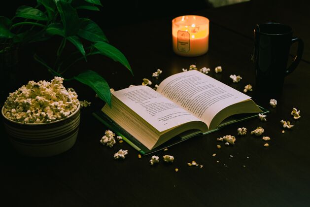 舒适一本打开的书的特写镜头 桌上放着一碗爆米花 点着蜡烛和一杯咖啡点燃蜡烛木头