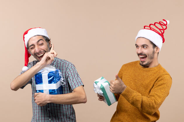 米色正面图：两个快乐的家伙在米色孤立的背景下交谈并拿着圣诞礼物成人视图头饰