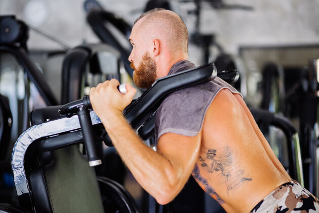 出汗适合纹身胡须男子做蹲在训练机蹲锻炼健美