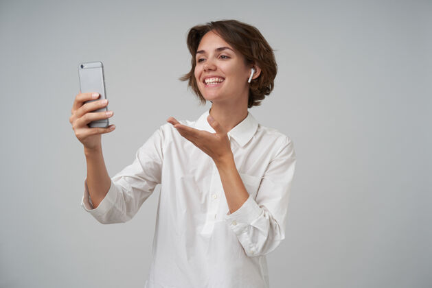 棕色积极漂亮的黑发女人 留着短发 用智能手机拍自己的照片 笑容满面 高兴地举起手掌 与世隔绝情绪心情短发