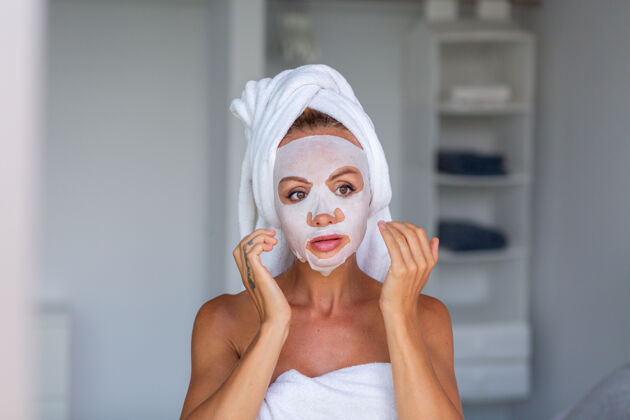 提举冷静的白人美女肖像 头上戴着毛巾 脸上戴着化妆面具 面部皮肤护理概念女性在家里的床上放松常规化妆品治疗