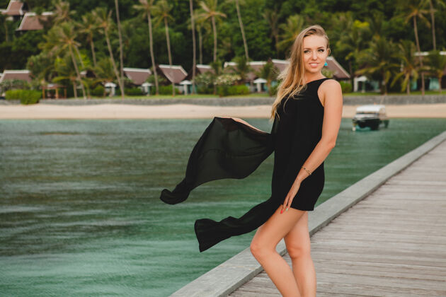 女性穿着黑色连衣裙的美丽迷人的女人在豪华度假酒店的码头上摆姿势 暑假 热带海滩度假胜地奢华优雅