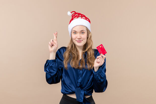 圣诞节正面图年轻女性手持红色银行卡 背景为粉色节日圣诞钱照片新年感慨年轻人银行帽子
