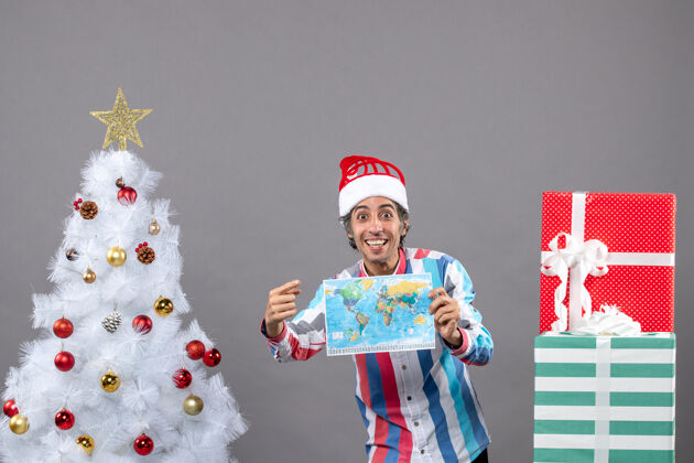 举行正面图：戴着螺旋弹簧圣诞帽的快乐男人指着拿着世界地图的东西地图春天帽子