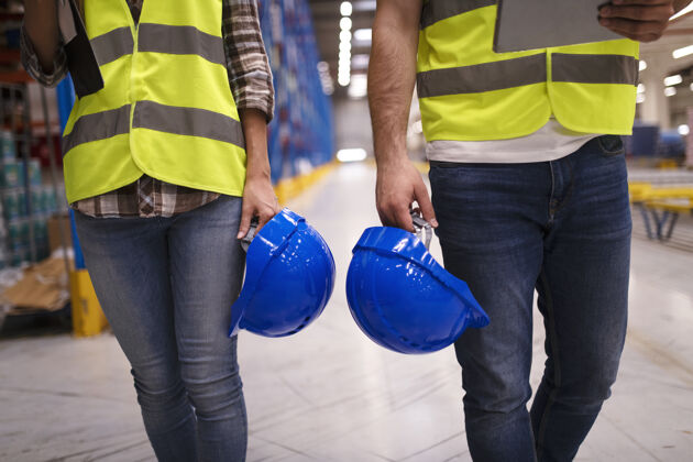 安全帽两个面目全非的工人穿着反光服 手持蓝色安全帽 穿过仓库妇女储存防护