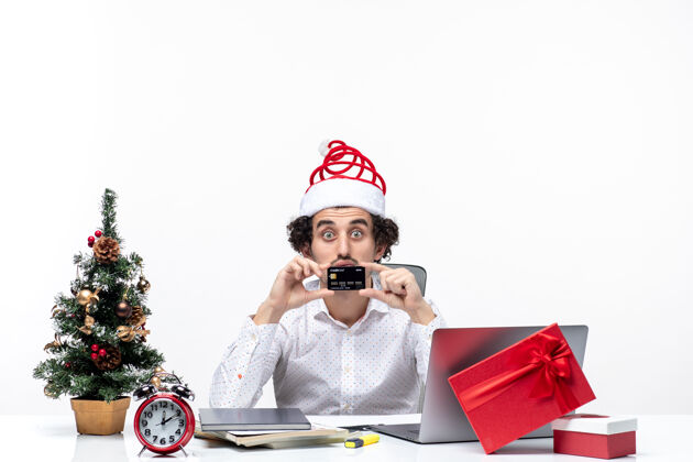 银行带着圣诞老人帽子 出示银行卡和在办公室的商务人士感到惊讶的节日气氛人商务人士圣诞节