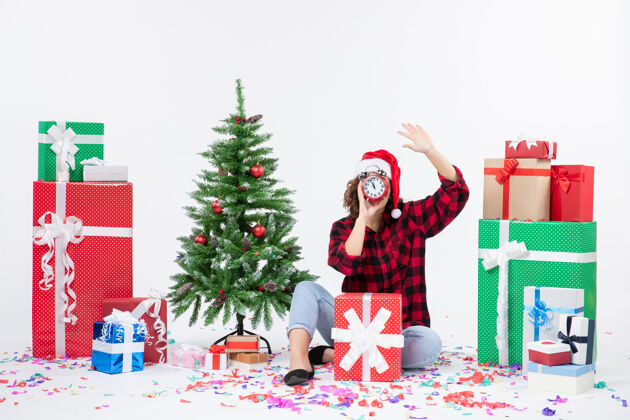 庆祝前视图的年轻女子坐在圣诞礼物周围拿着白色墙上的时钟前面十二月时钟