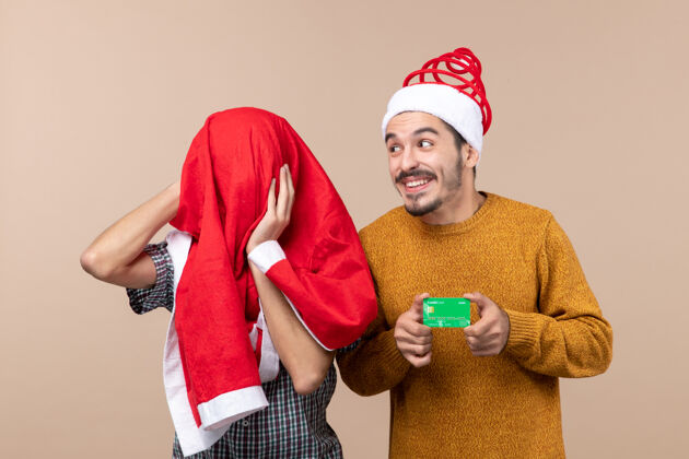 两个伙计们前视图两个家伙一个拿着信用卡 另一个用圣诞老人的外套盖着他的头 背景是米色的卡片米色男人