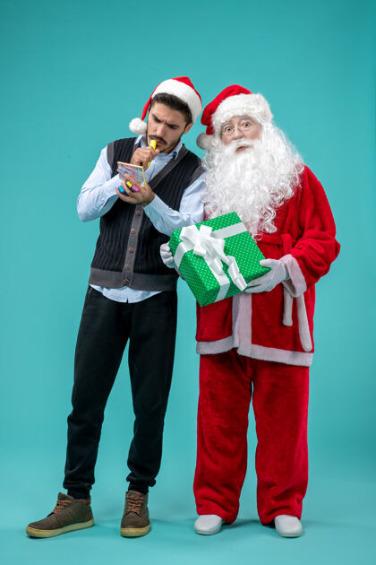 笔记前视图：圣诞老人和正在蓝色背景上做笔记的年轻男性前面圣诞老人乐器