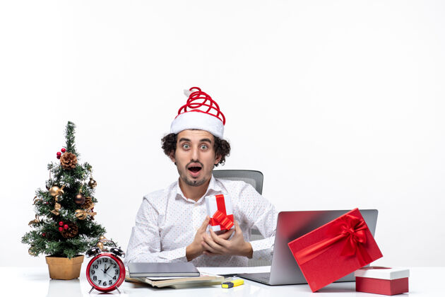 微笑圣诞节心情与震惊兴奋的年轻商人圣诞老人帽子和举行他的礼物头脑风暴在白色背景帽子成人礼物
