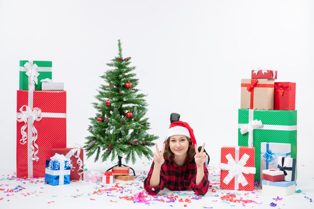 雪年轻女子躺在白色墙壁上的圣诞礼物和小圣诞树周围的正视图小装饰前面