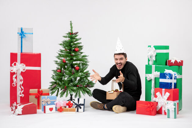 礼物年轻人坐在白色墙壁上的节日礼物周围的正面视图快乐模型树