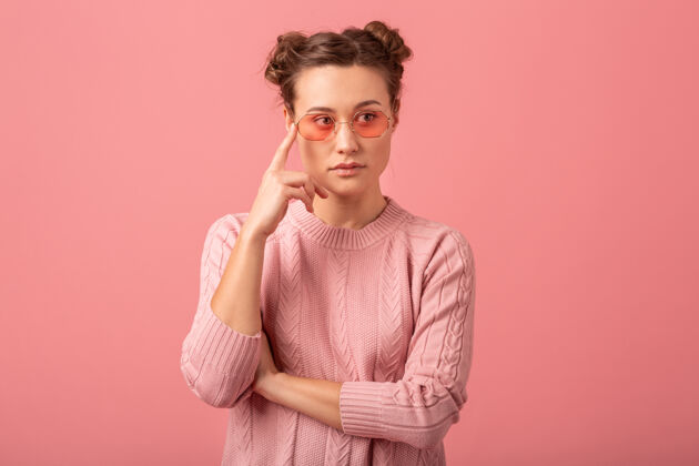 思考在粉红色的工作室背景上 一个穿着粉色毛衣 戴着太阳镜的年轻漂亮有思想的女人的特写肖像思考淑女想法