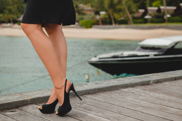 天堂双腿穿着黑色高跟鞋的奢华性感迷人的女人穿着黑色礼服摆在码头上的豪华度假酒店 暑假 热带海滩女孩船魅力