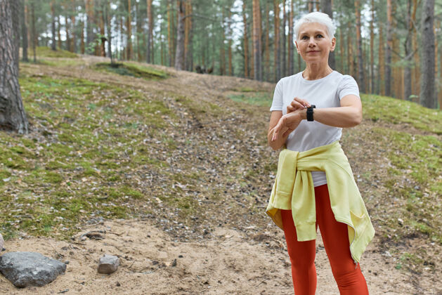 腕部户外肖像自信活跃的中年女性在运动服使用智能手表监测脉搏或心率 而在公园锻炼技术慢跑健康