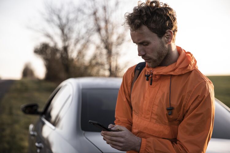 男性在户外使用智能手机进行公路旅行的男人的前视图旅行远足户外