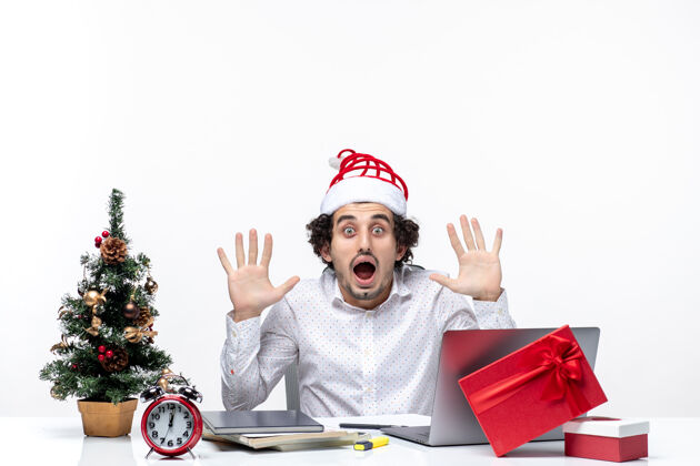 某人震惊的年轻商人戴着滑稽的圣诞老人帽子 看着办公室里白色背景的人礼物圣诞节看