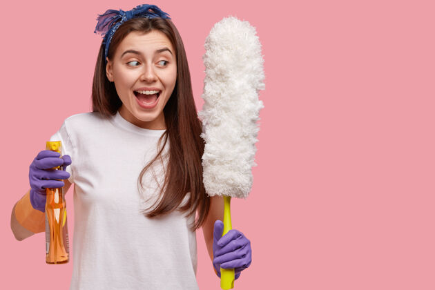 女佣积极的欧洲女人戴着手套和头带 高兴地看着旁边 拿着喷雾和刷子打扫房间家务积极服装