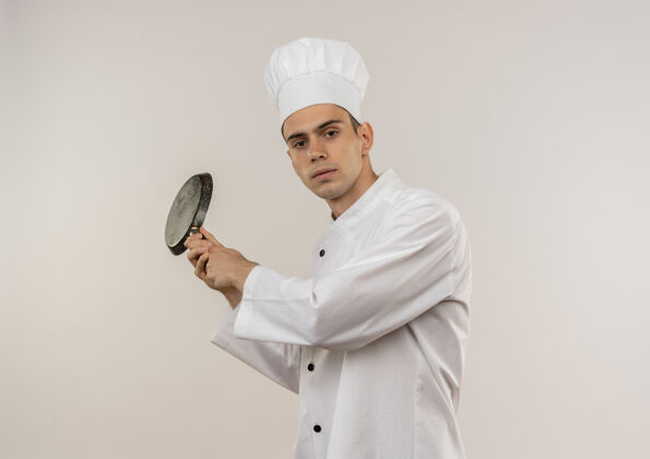穿着年轻的男厨师穿着厨师制服 肩上扛着煎锅 站在孤零零的白墙上制服围着平底锅