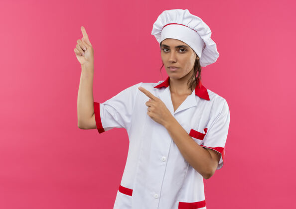 厨师穿着厨师制服的年轻女厨师点到一边 在隔离的粉色墙壁上留有临摹空间边年轻制服