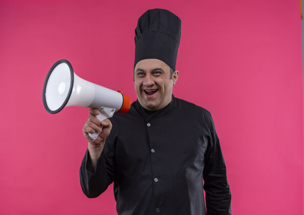 制服身着厨师制服的快乐中年男厨师在孤立的粉红色墙上通过扬声器讲话厨师喇叭快乐