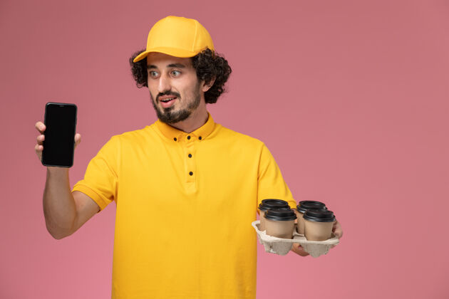 快递员正面图身穿黄色制服的男信使手拿棕色咖啡杯 粉色墙上挂着电话男性男士视野
