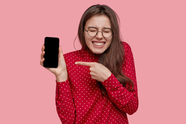 指向乐观的白种女人指着新的智能手机做广告 显示空白屏幕 喜欢多功能小玩意女士展示技术