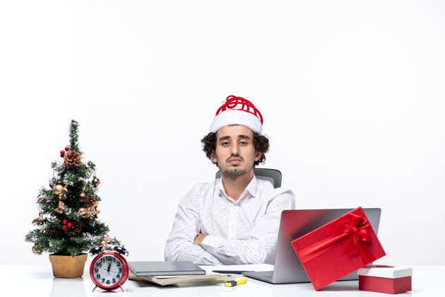 电脑忙碌严肃的年轻商人戴着滑稽的圣诞老人帽子在白色背景的办公室里摆姿势拍照笔记本电脑年轻圣诞节