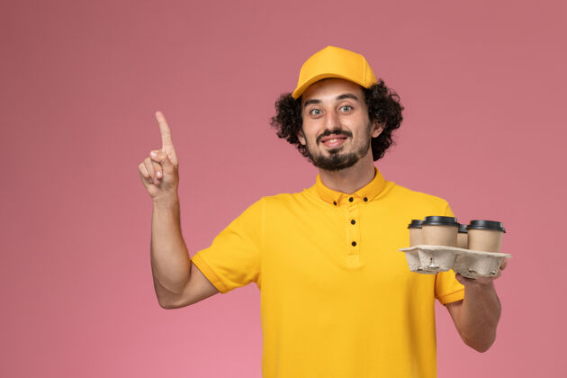 快递员正面图穿着黄色制服的男信使拿着棕色的咖啡杯在粉红色的墙上工作男性职业