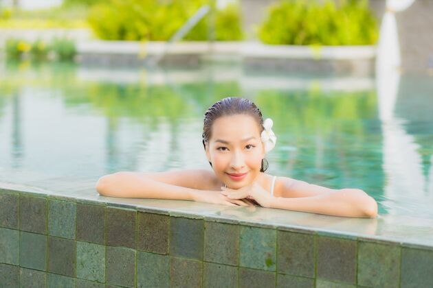 享受肖像美丽的亚洲年轻女子放松微笑周围的室外游泳池在酒店度假村日光浴水豪华