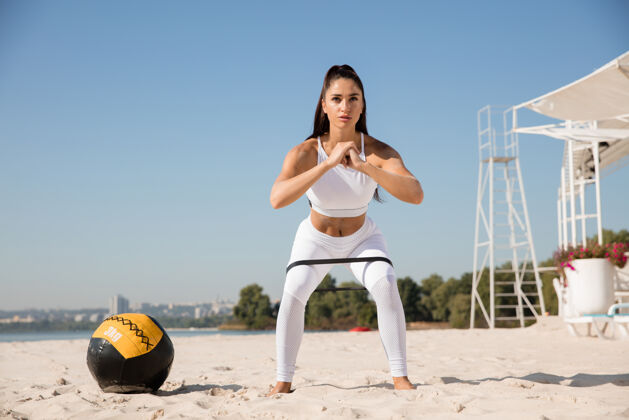 身体年轻健康的女人在沙滩上拿着球蹲着户外成年人女人