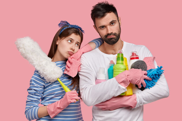清洁剂室内拍摄的不悦男女用抹布 化学清洁剂和刷子打扫房间 都有沮丧凄惨的表情没有刮胡子家庭家庭主妇