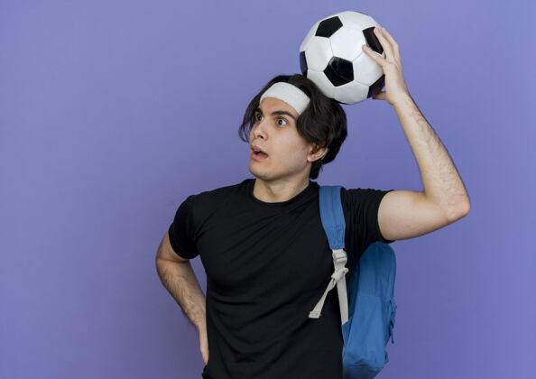 背包一个穿着运动服 头戴头巾 背着背包 头上顶着足球的年轻人 困惑而惊讶地看着一边运动装运动困惑