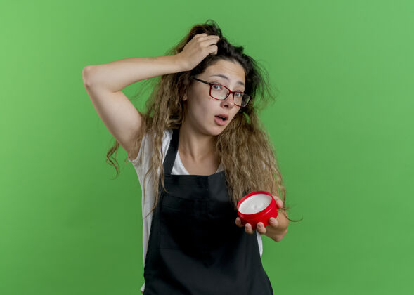 困惑年轻的专业美发师女士围着围裙拿着一罐发膏 用手误按在头上女人绿色错误