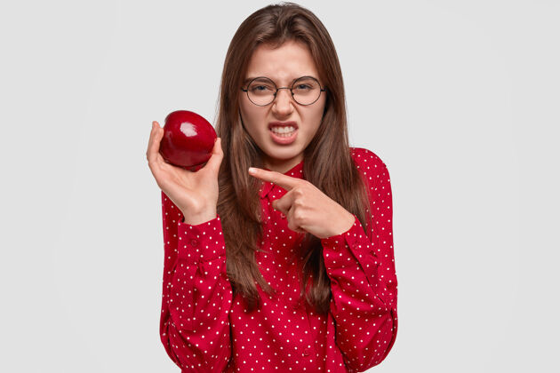 表示不高兴的黑发女人咬紧牙关 不满地皱眉 拿着苹果 不喜欢它的味道维生素指不高兴