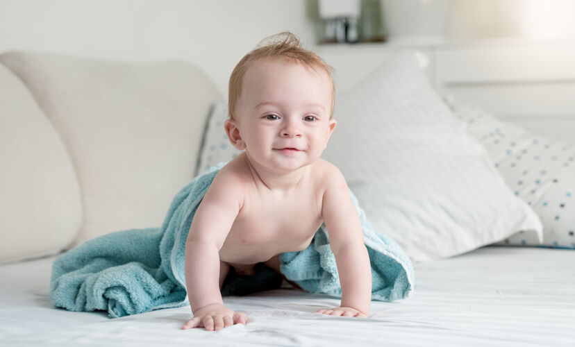 毯子美丽的9个月大的婴儿沐浴后在蓝色毛巾上爬在床上儿子玩谎言