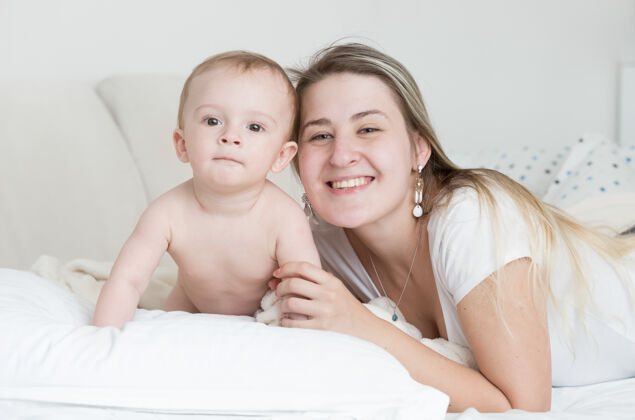 快乐快乐微笑的男婴和母亲躺在枕头上的特写肖像谎言无忧无虑玩耍