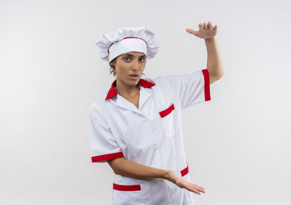 尺寸穿着厨师制服的年轻女厨师在隔离的白色墙壁上展示尺寸 并留有复印空间年轻厨师厨师